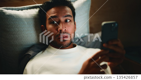 Night, surprise and man with phone in bedroom, watch horror movie and loud noise for fear reaction. Shock, suspicious sound and person in dark home with mobile for film streaming, worry and paranoid 135426857