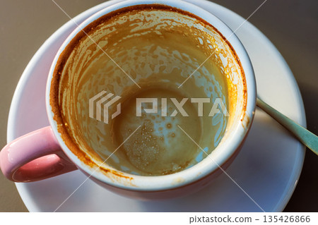 Empty coffee cup with latte residue on saucer and spoon in sunlight Empty coffee cup with latte residue on saucer and spoon in sunlight 135426866