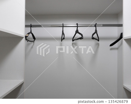 Empty white closet interior with black hangers on a metal rod. Wardrobe storage background with copy space 135426879