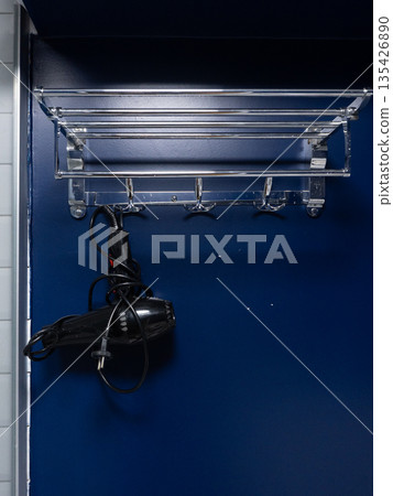 Chrome towel rack with hanging black hair dryer on blue wall. Bathroom interior organization and storage concept. Vertical photo with copy space 135426890