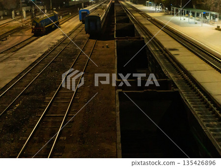 Railway station at night with freight wagons and diesel locomotive. High angle view of industrial rail yard tracks and empty platform 135426896