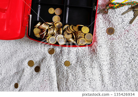 Open red cash box on textile bed blanket with scattered coins Open red cash box on textile bed blanket with scattered coins 135426934