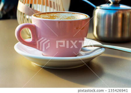 Empty pink coffee cup with latte residue on saucer with spoon and blurred decor behind on sunlit cafe table Empty pink coffee cup with latte residue on saucer with spoon and blurred decor behind on sunlit cafe table 135426941
