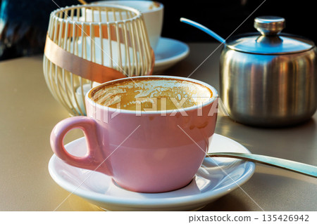 Empty pink coffee cup with latte residue on saucer with spoon and blurred decor behind on sunlit cafe table Empty pink coffee cup with latte residue on saucer with spoon and blurred decor behind on sunlit cafe table 135426942