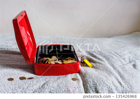 Open red cash box on textile bed blanket with scattered coins 135426968