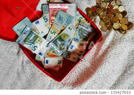 Overhead view of open red cash box filled with euro banknotes and coin pile Overhead view of open red cash box filled with euro banknotes and coin pile 135427033