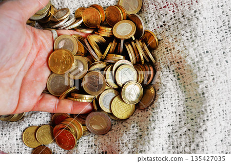 Close up of euro coins slipping through a fingers. Scattered change on the bed blanket. Close up of euro coins slipping through a fingers. Scattered change on the bed blanket. 135427035