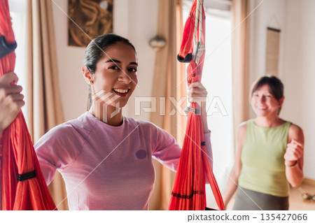 Young latin woman smiling practicing aerial yoga Young latin woman smiling practicing aerial yoga 135427066
