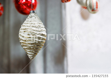 A closeup of gloden silver textured pinecone Christmas ornament and red baubles at blurred background. Holiday display with Xmas and new year decoration. Neutral tones and shallow depth of field. A closeup of gloden silver textured pinecone Christmas ornament and red baubles at blurred background. Holiday display with Xmas and new year decoration. Neutral tones and shallow depth of field. 135427155