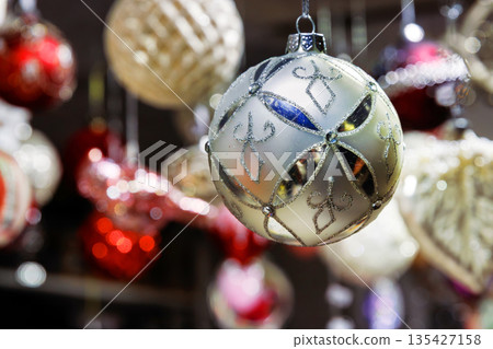 Glass christmas ornaments hanging in a decorative display at a holiday market stall. Closeup with a softly blurred background. Glass christmas ornaments hanging in a decorative display at a holiday market stall. Closeup with a softly blurred background. 135427158