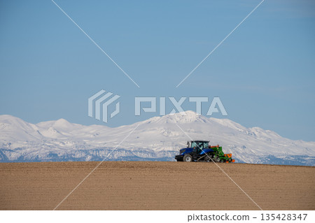 Tractor plowing a spring field and snowy mountains 135428347