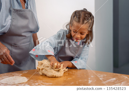 Girl kneading dough on table while baking with Girl kneading dough on table while baking with 135428523