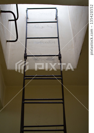 View of a metal ladder leading to a small, illuminated opening above View of a metal ladder leading to a small, illuminated opening above 135428552
