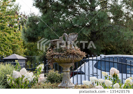 Fountain with birds surrounded by flowers and trees in a suburban garden during 135428576