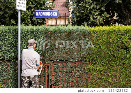 Gardener trimming hedge under Nadmorska street sign in a residential area 135428582