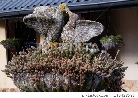 Stone fountain with bird sculptures and blooming greenery in a peaceful Stone fountain with bird sculptures and blooming greenery in a peaceful 135428585