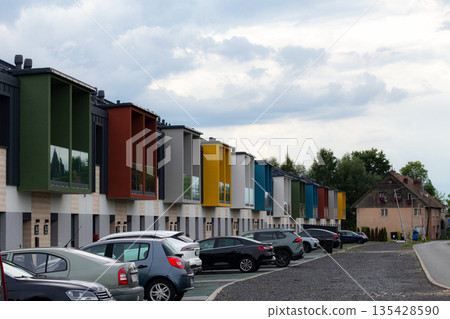 Colorful modern townhouses line a quiet street on an overcast day with parked cars nearby 135428590