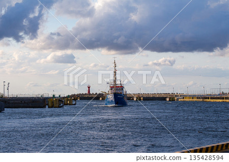 Coastal vessel navigating through a harbor entrance under a cloudy sky Coastal vessel navigating through a harbor entrance under a cloudy sky 135428594