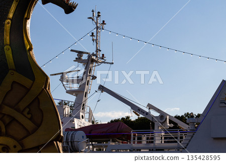 Coastal view with ship's deck, masts, and overhead lights during sunset Coastal view with ship's deck, masts, and overhead lights during sunset 135428595