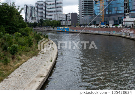 Urban river scene with modern buildings and graffiti under cloudy sky Urban river scene with modern buildings and graffiti under cloudy sky 135428624