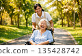 A foreign caregiver and an elderly Japanese patient stroll through the park in the soft sunlight, smiling. 135428742