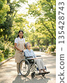 A foreign caregiver and an elderly Japanese patient stroll through the park in the soft sunlight, smiling. 135428743