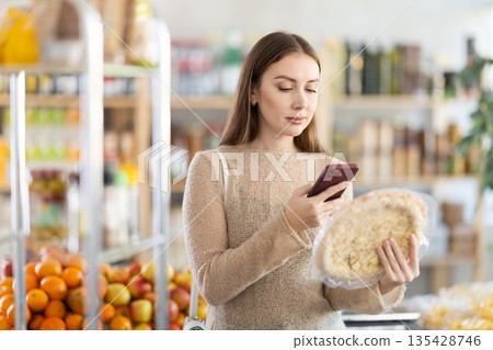 In shop young woman scans QR code and take reading on cheese pizza package using phone camera 135428746