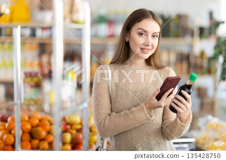 Young pretty girl buyer looking for soy sauce from photo on internet in store, scanning QR Young pretty girl buyer looking for soy sauce from photo on internet in store, scanning QR 135428750