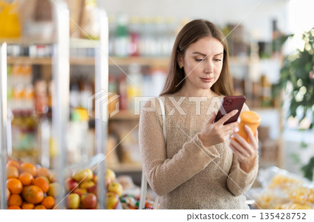 Smiling young girl shopper carefully examining mayonnaise on shelves of food store, scan QR code Smiling young girl shopper carefully examining mayonnaise on shelves of food store, scan QR code 135428752