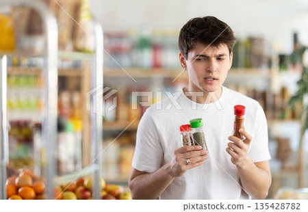 Guy examining bottles of spice bottles at grocery store Guy examining bottles of spice bottles at grocery store 135428782