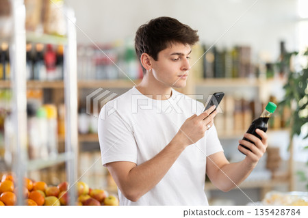 Guy scanning barcode on soy sauce using phone in food store Guy scanning barcode on soy sauce using phone in food store 135428784