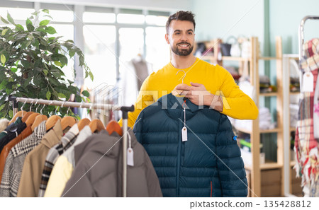 Young man choosing down jacket in clothing store Young man choosing down jacket in clothing store 135428812