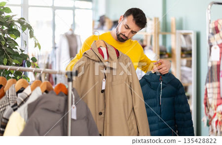 Man choosing a jacket of his size in a clothing store Man choosing a jacket of his size in a clothing store 135428822