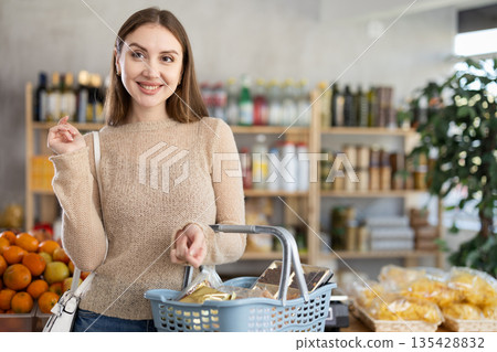 Young female shopper walking with shopping basket in grocery store Young female shopper walking with shopping basket in grocery store 135428832