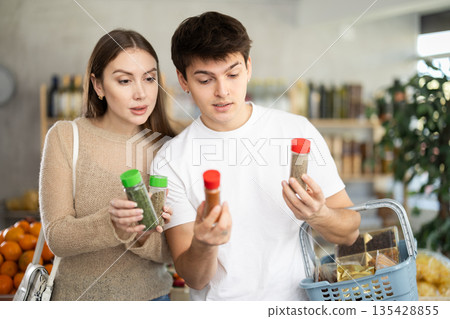 Pretty young wife tells her husband what delicious spices and seasonings to buy in supermarket Pretty young wife tells her husband what delicious spices and seasonings to buy in supermarket 135428855