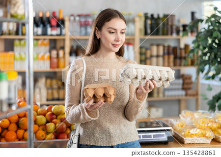 Young beautiful woman shopper in casual clothes chooses package of eggs in supermarket 135428861