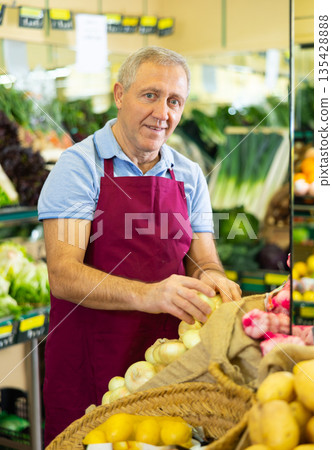 Professional old male seller putting onion on shelves in grocery shop 135428888