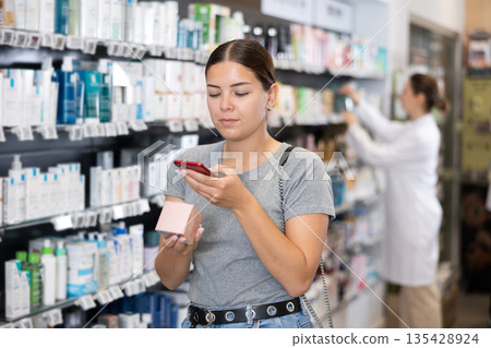 Woman customer using phone to search information about selected product at pharmacy Woman customer using phone to search information about selected product at pharmacy 135428924