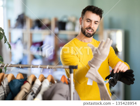 Young man choosing and trying on gloves in clothing store Young man choosing and trying on gloves in clothing store 135428954