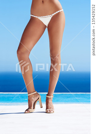 Legs, woman and bikini body closeup with heels at beach, ocean and waves or tan, skin and high shoes. Summer fashion, beauty or travel and pool, sea and spa or female model, wellness and blue sky 135429152
