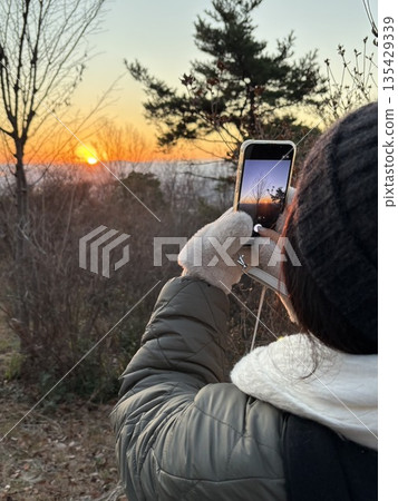 Woman taking a picture of the sunrise Woman taking a picture of the sunrise 135429339