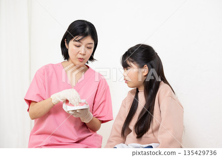 A dental hygienist uses a model to teach a child patient how to brush their teeth. A dental hygienist uses a model to teach a child patient how to brush their teeth. 135429736
