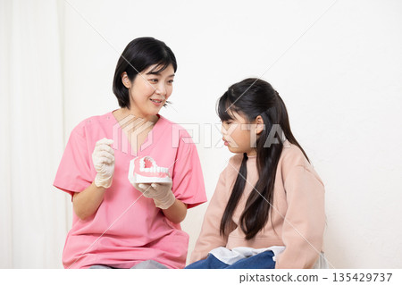 A dental hygienist uses a model to teach a child patient how to brush their teeth. A dental hygienist uses a model to teach a child patient how to brush their teeth. 135429737