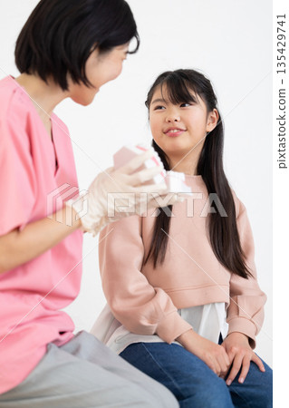An elementary school girl being taught how to brush her teeth by a dental hygienist 135429741