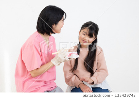An elementary school girl being taught how to brush her teeth by a dental hygienist 135429742