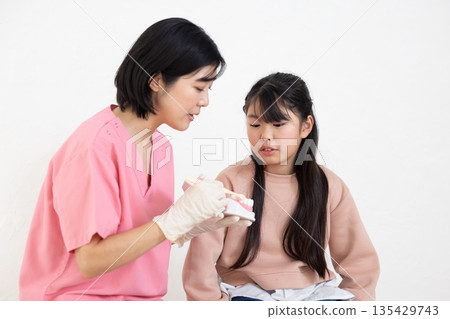牙齒保健員使用模型教導小患者如何刷牙。 牙齒保健員使用模型教導小患者如何刷牙。 135429743