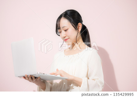 年輕女子在粉紅色背景下用筆記型電腦打字 135429995