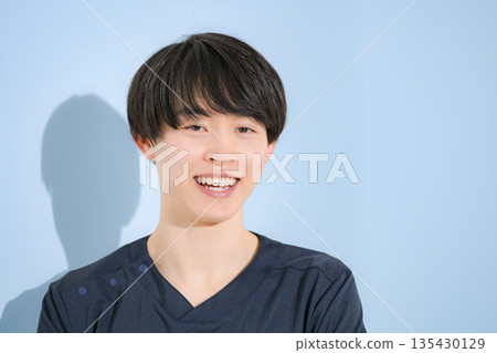 一位年輕的男護士或醫生穿著手術服,站在淺藍色背景前,微笑著看著鏡頭。 一位年輕的男護士或醫生穿著手術服,站在淺藍色背景前,微笑著看著鏡頭。 135430129
