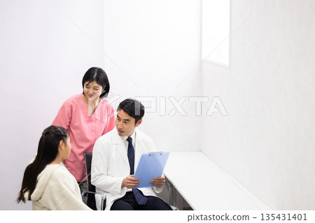 A male doctor examining an elementary school student patient and a female nurse supporting him 135431401