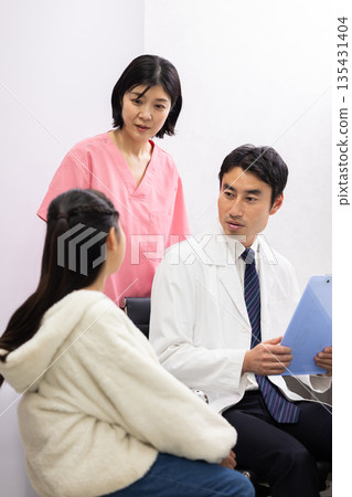 A male doctor examining an elementary school student patient and a female nurse supporting him A male doctor examining an elementary school student patient and a female nurse supporting him 135431404